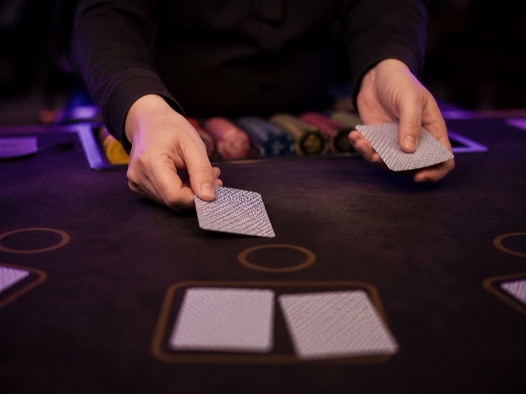 Le mani di un croupier distribuiscono carte coperte su un tavolo da gioco scuro illuminato di viola
