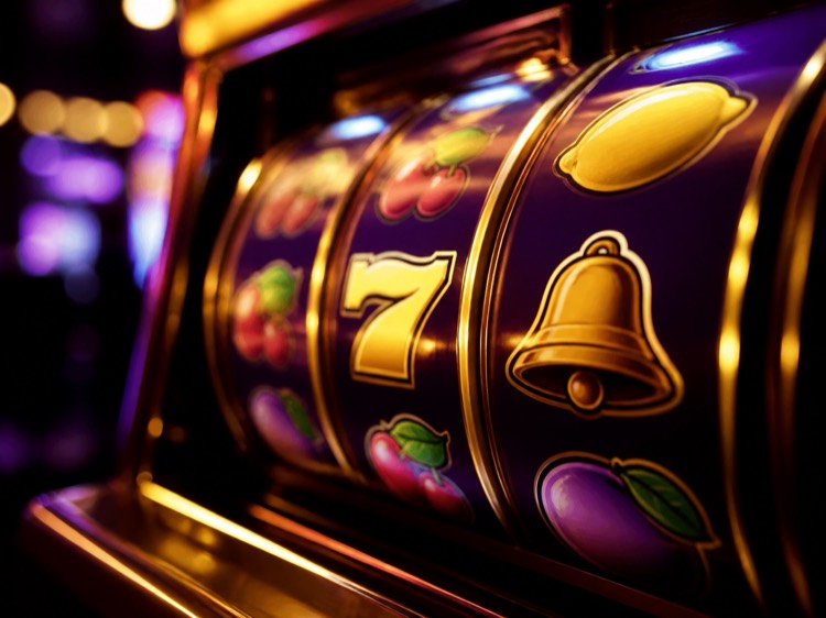 Primo piano dei rulli di una slot machine con simboli dorati, campana e sette, illuminati di viola